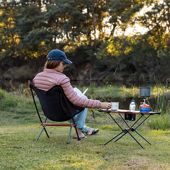 femme qui boit son café en plein camping avec une chaise à ses cotés