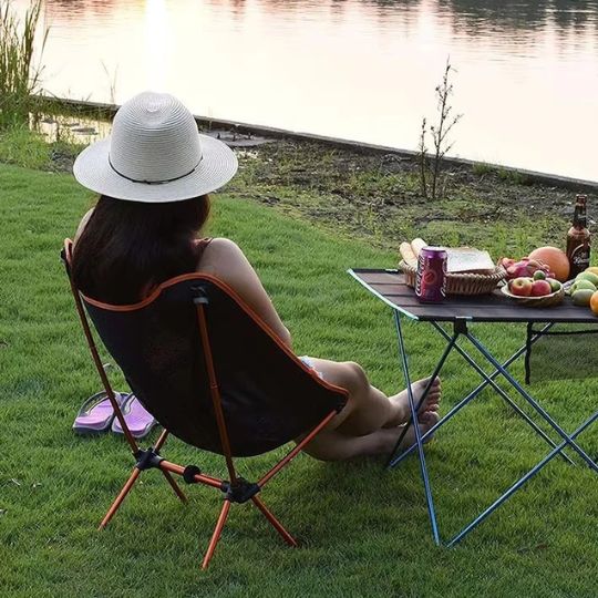 chaise-de-camping-orange-avec-femme-assise-pres-de-lac