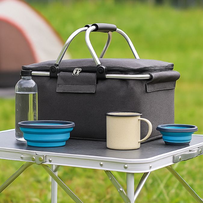 une glaciere souple noir sur une table de camping en nature accompagnée de bol pliable 