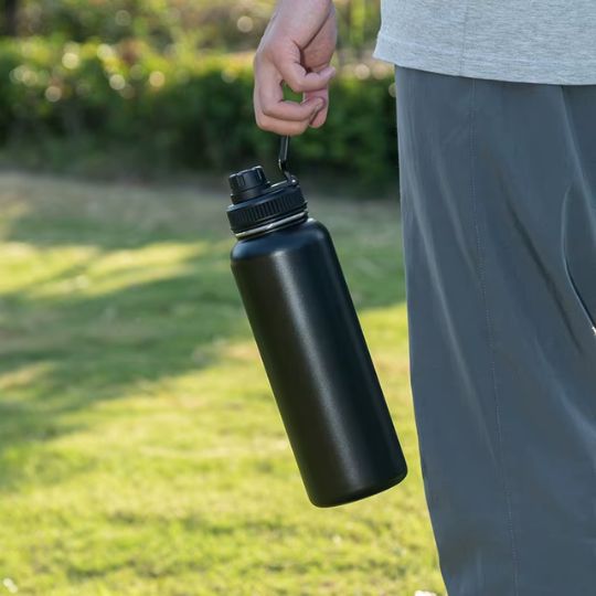 personne qui tient une gourde 1l noir dehors par la anse