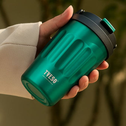une personne qui tient un mug café isotherme vert dans sa main