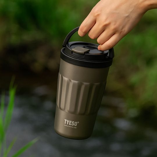 un mug café isotherme gris tenu par anse deployable