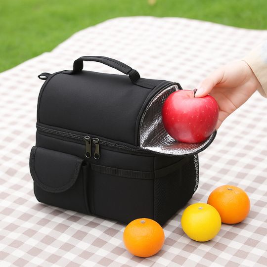 Présentation d'une main qui met une pomme dans le haut d'un sac repas isotherme