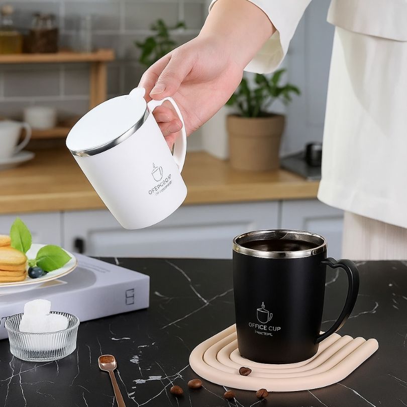 personne qui tient une tasse isotherme blanche par l'anse