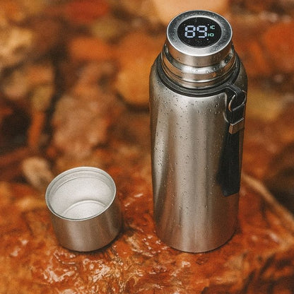 un thermos isotherme argenté sur un rocher avec son bouchon tasse à coté
